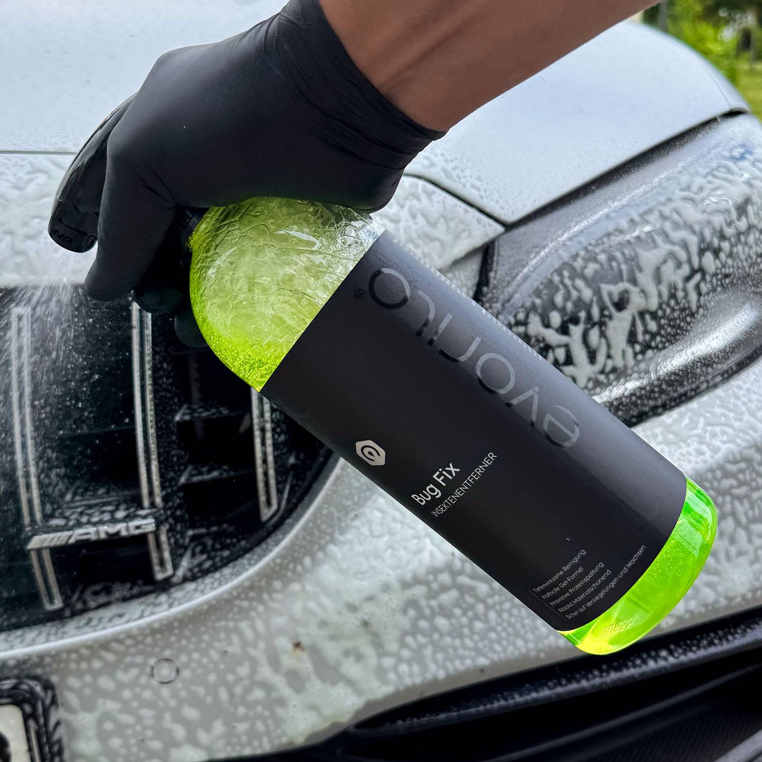 Hand hält evorilo Bug Fix Insektenentferner vor nasser Autostoßstange für effektive Reinigung.