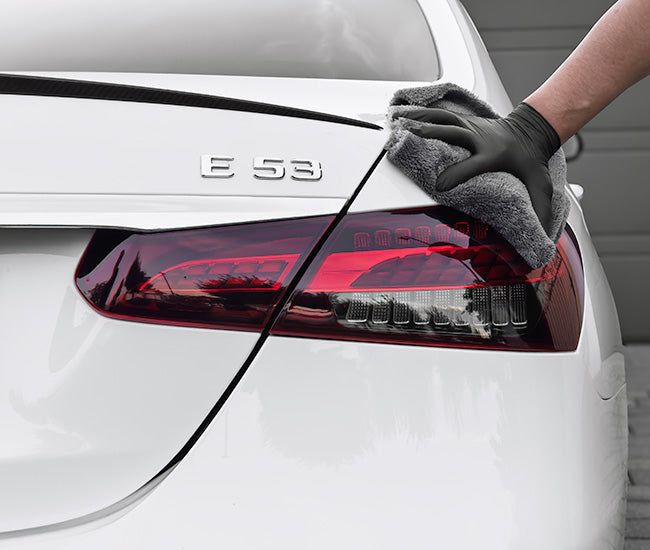 Lackpflege am Heck eines weißen Fahrzeugs mit Mikrofasertuch